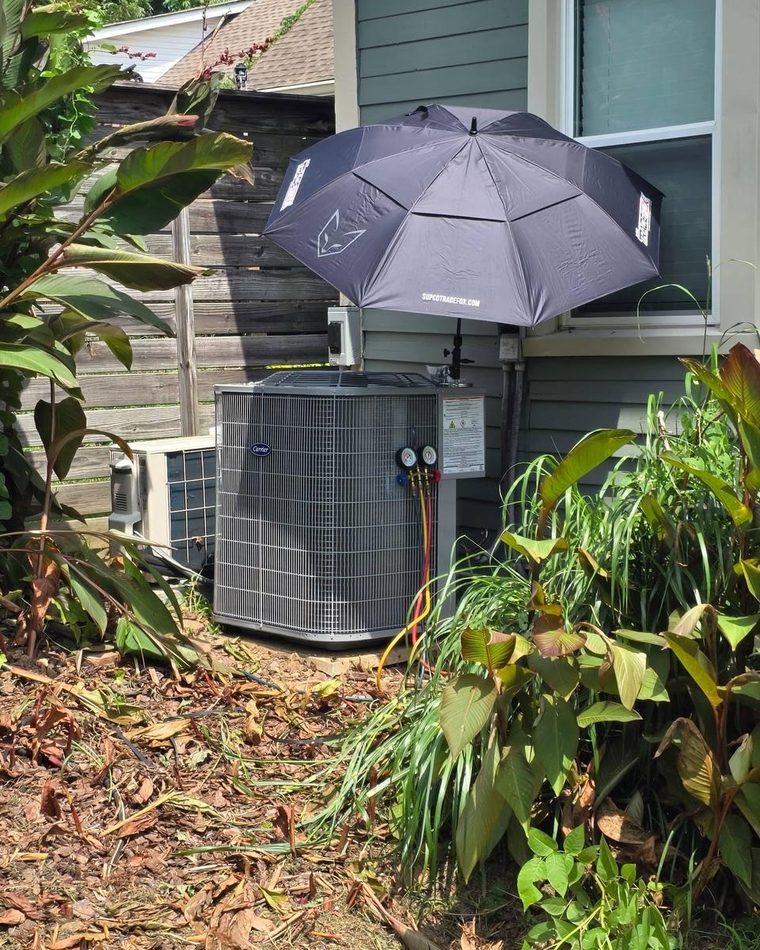 A Carrier condenser under a service umbrella with the gauges connected, beside a house