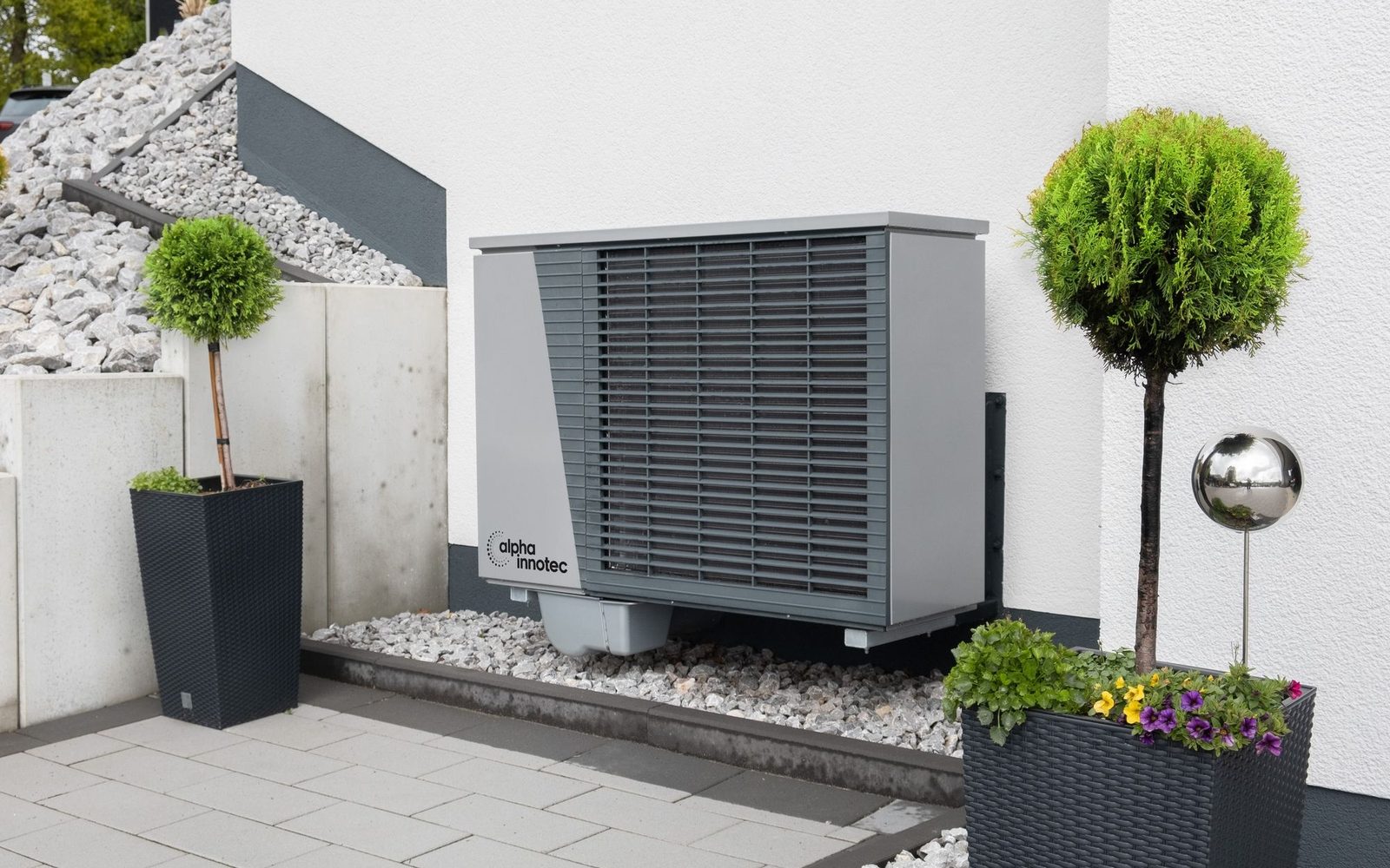 A condenser beside a building wall under trees